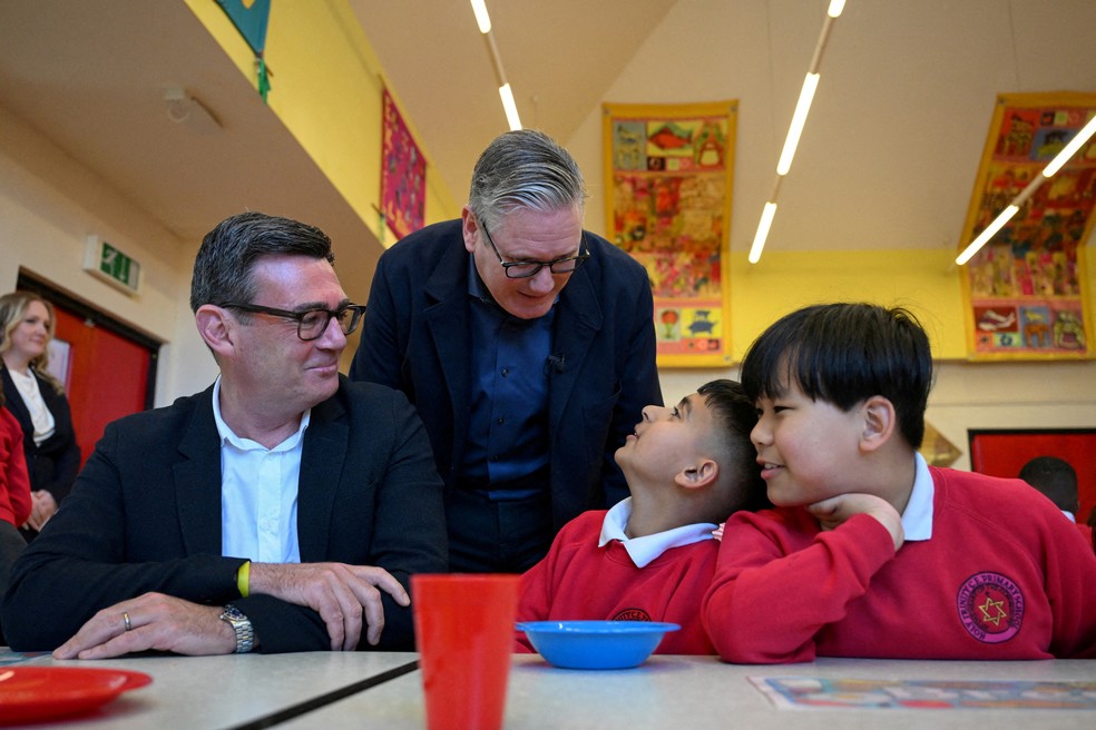 Andy Burnham, sentado à mesa com crianças, ao lado de Keir Starmer — Foto: PAUL ELLIS/Pool via REUTERS