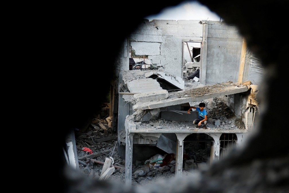 Um menino palestino sentado em uma casa danificada vista através dos escombros, após os ataques israelenses, em Khan Younis, no sul da Faixa de Gaza, 11 de outubro de 2023 — Foto: REUTERS/Ibraheem Abu Mustafa