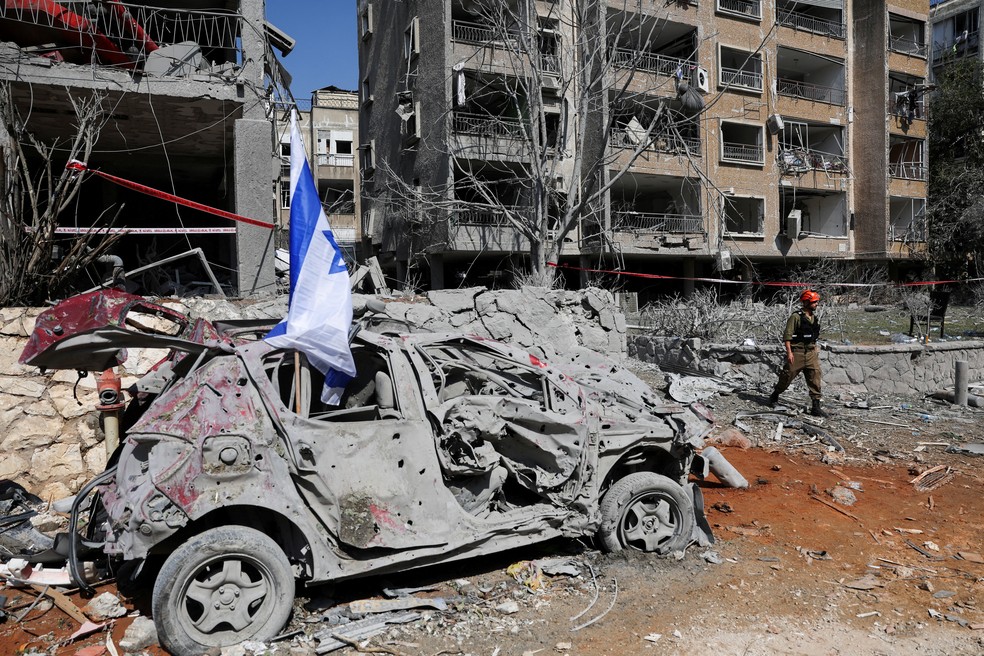 Uma equipe de resgate caminha ao lado de um veículo danificado no local do impacto após um ataque de mísseis do Irã contra Israel, em Ramat Gan, Israel, em 14 de junho de 2025 — Foto: REUTERS/Ronen Zvulun/Arquivo