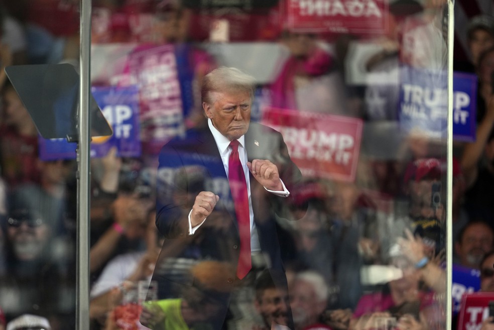 O ex-presidente republicano Donald Trump dança atrás de um vidro blindado que reflete apoiadores em um comício de campanha em Gastonia, Carolina do Norte — Foto: Chris Carlson/AP