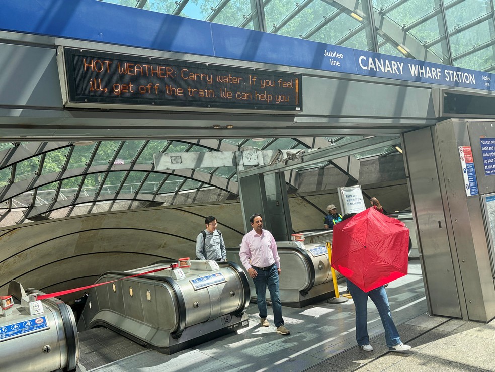 Passageiros do metrô passam por baixo de painéis de LED com mensagens de saúde sobre o calor em frente à estação de metrô Canary Wharf, em Londres — Foto: REUTERS/Suzanne Plunkett