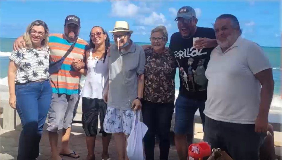 Hugo, seus familiares e a equipe médica de cuidados paliativos estão em frente ao mar de Recife comemorando a realização do sonho do idoso de voltar para sua terra natal.