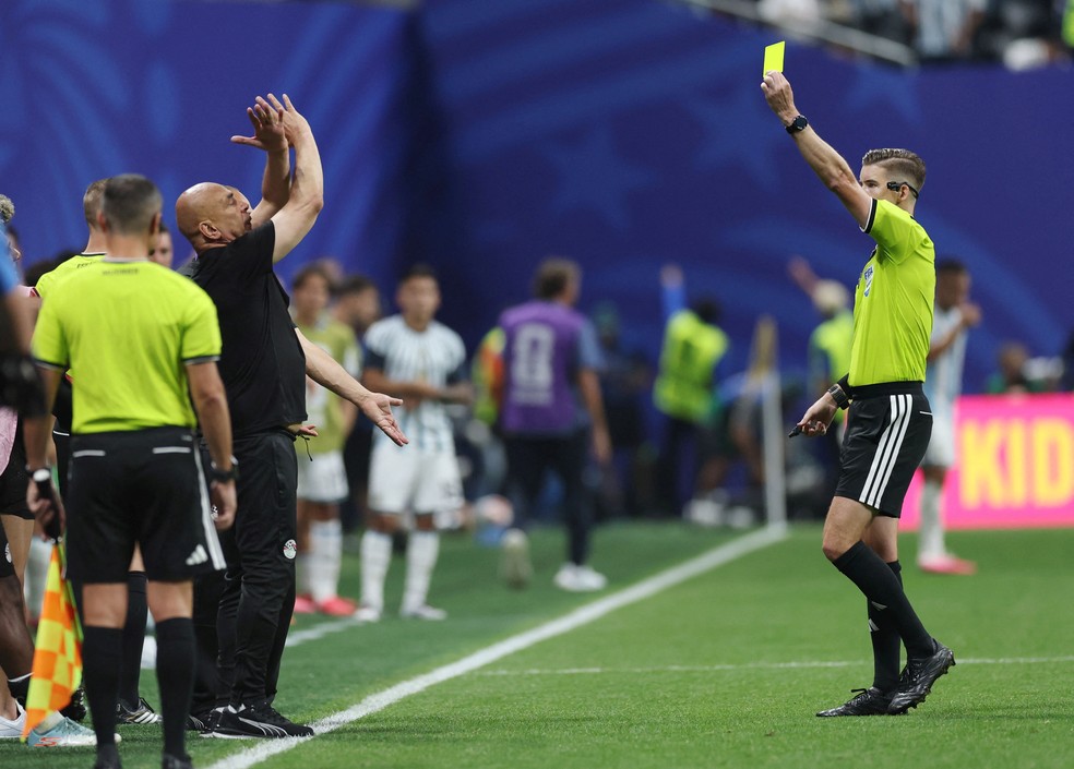 O técnico do Egito, Hossam Hassan, recebe o cartão amarelo do árbitro François Letexier enquanto faz um gesto contra o racismo durante jogo contra a Argentina. — Foto: Reuters/Paul Childs