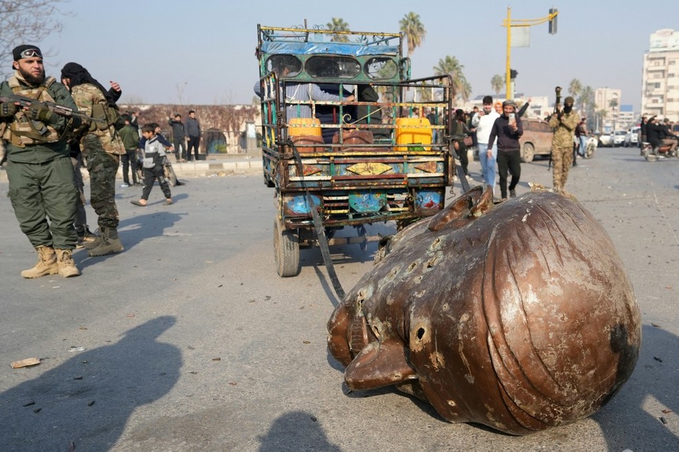 Cabeça de estátua de Hafez al-Assad, ex-presidente da Síria e pai do atual presidente Bashar, é rebocada por caminhão em Hama, cidade tomada por rebeldes, em 6 de dezembro de 2024. — Foto: Muhammad Haj Kadour/AFP
