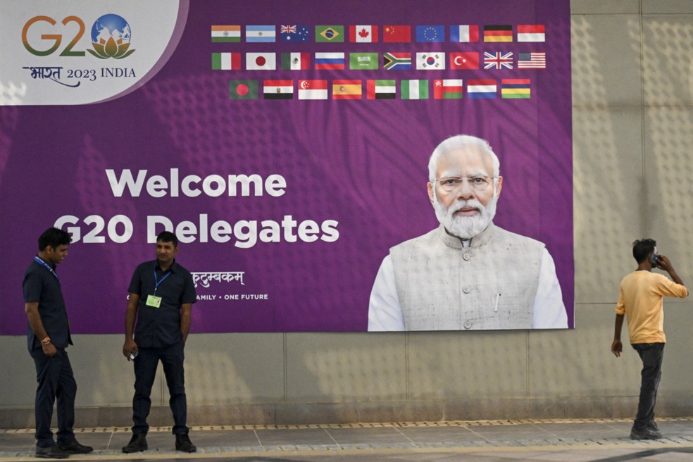 Funcionários em frente a outdoor do G20, que mostra o primeiro-ministro indiano Narendra Modi com os dizeres "bem-vindos, delegados do G20". Reunião do grupo acontece neste final de semana em Nova Delhi. — Foto: Tauseef Mustafa/AFP