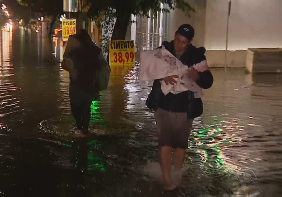 André Wagner Trindade carregando a filha de colo por rua alagada de Canoas — Foto: RBS TV/Reprodução