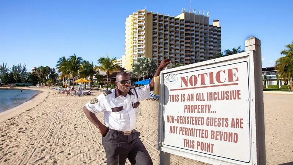 Segurança em uma praia, ao lado de uma placa avisando que se trata de propriedade particular e apenas hóspedes autorizados podem ultrapassar o aviso. — Foto: Alamy via BBC