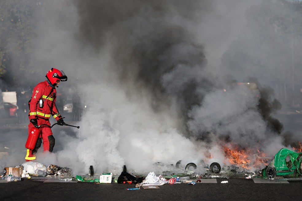 Um bombeiro francês apaga latas de lixo e objetos em chamas colocados por estudantes para bloquear o tráfego próximo ao colégio Lycée Hélène Boucher durante um dia de protestos em Paris, como parte de um movimento de protesto popular chamado 'Bloquons Tout' ('Vamos Bloquear Tudo') — Foto: Benoit Tessier/Reuters