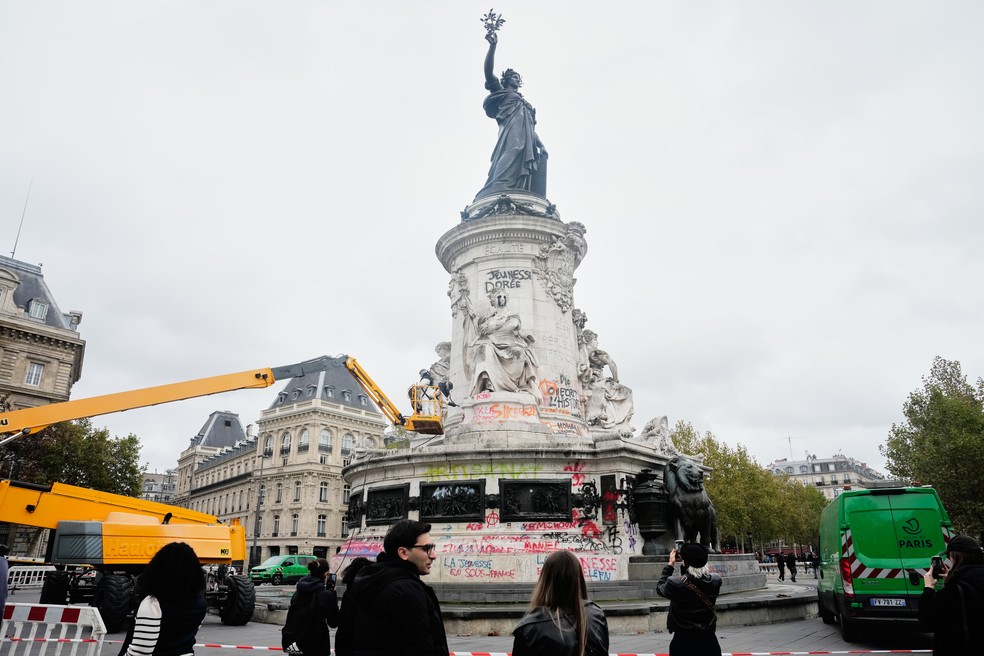Pessoas observam e tiram fotos dos trabalhos de limpeza em Paris após protestos contra o custo de vida, no fim de semana, terminarem em tumultos e saques em várias partes da França. — Foto: Teresa Suarez / AP