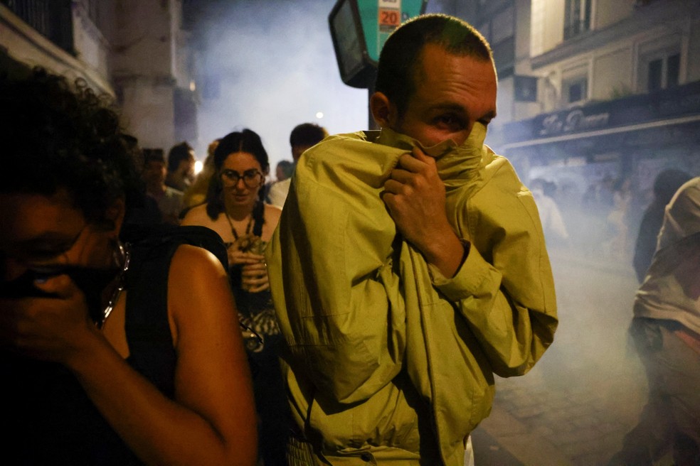 Pessoas se protegem do gás lacrimogênio durante ato em Paris após resultado do 1° turno — Foto: Fabrizio Bensch/Reuters
