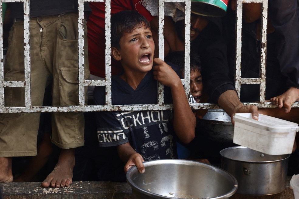 Crianças palestinas esperam por uma refeição em uma cozinha de caridade na área de Mawasi, em Khan Yunis, no sul da Faixa de Gaza, em 22 de julho de 2025 — Foto: AFP