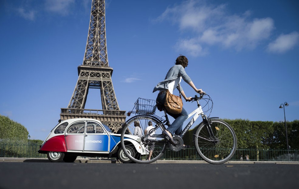Ciclista passa por um antigo Citron 2CV pintado com as cores da bandeira francesa, estacionado em frente  Torre Eiffel, em Paris.  Foto: Fred Dufour/AFP