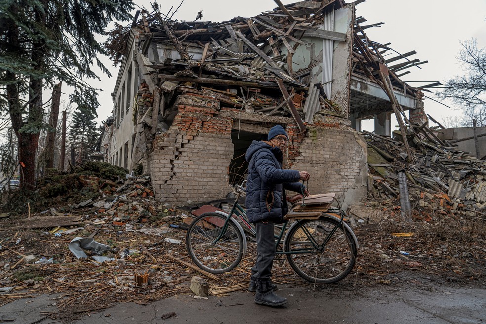 Idoso amarra lenha em sua bicicleta em frente a um prédio danificado por ataques militares russos, em meio à ofensiva da Rússia contra a Ucrânia, em Pokrovsk, na região de Donetsk, na Ucrânia. — Foto: REUTERS/Anton Shynkarenko