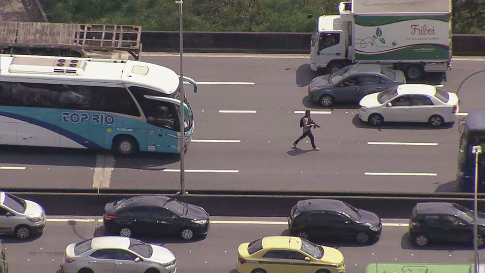 Na contramão, policial civil escolta um dos ônibus escolares usado como barricada na Linha Vermelha — Foto: Allan Cavalcante /TV Globo