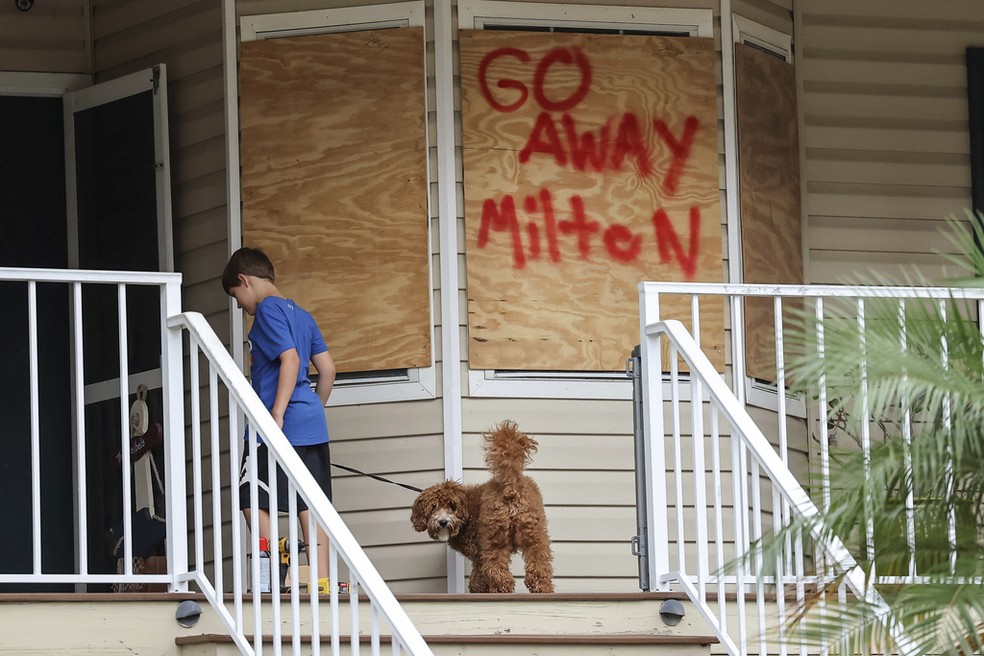 Menino caminha diante de inscrição 'Vá embora, Milton', em referência ao furacão Milton, em Port Richey, na Flórida, nos EUA, em 7 de outubro de 2024. — Foto: Mike Carlson/ AP