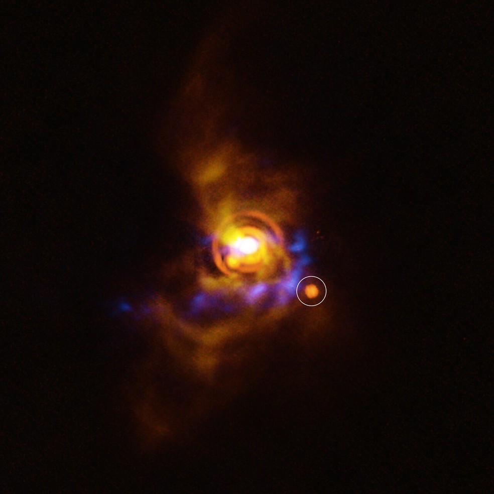 Imagem mostra possvel companheiro ao redor da jovem estrela V960 Mon, a mais de 5 mil anos-luz. A estrutura foi observada com o VLT (em laranja), sobreposta a dados anteriores do SPHERE (amarelo) e do ALMA (azul).  Foto: ESO/A. Dasgupta/ALMA (ESO/NAOJ/NRAO)/Weber et al.