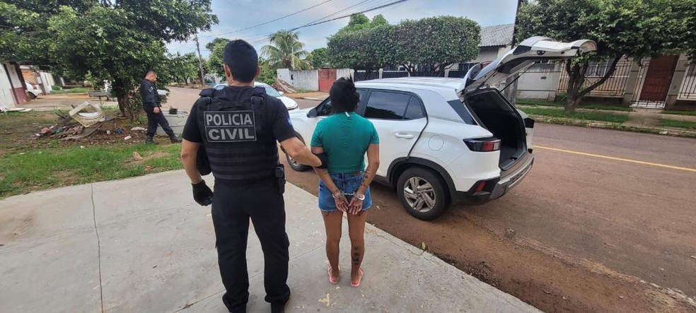 Policial levando um dos alvos presos algemados — Foto: Polícia Civil de Mato Grosso