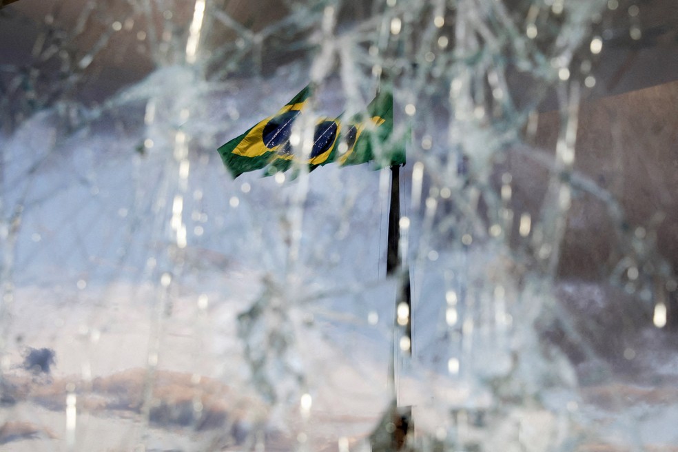 8 de janeiro - A Bandeira Nacional é vista tremulando atrás de vidros vandalizados no prédio do Supremo Tribunal Federal, após os atos antidemocráticos do 8 de Janeiro em Brasília — Foto: Ricardo Moraes/Reuters