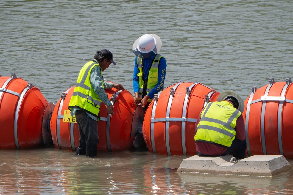 Nesta imagem de agosto, trabalhadores fazem a manutenção da barreira de boias instalada pelo governo do Texas no Rio Grande, fronteira natural entre os EUA e o México, para impedir a passagem de imigrantes. — Foto: Suzanne Cordeiro/AFP