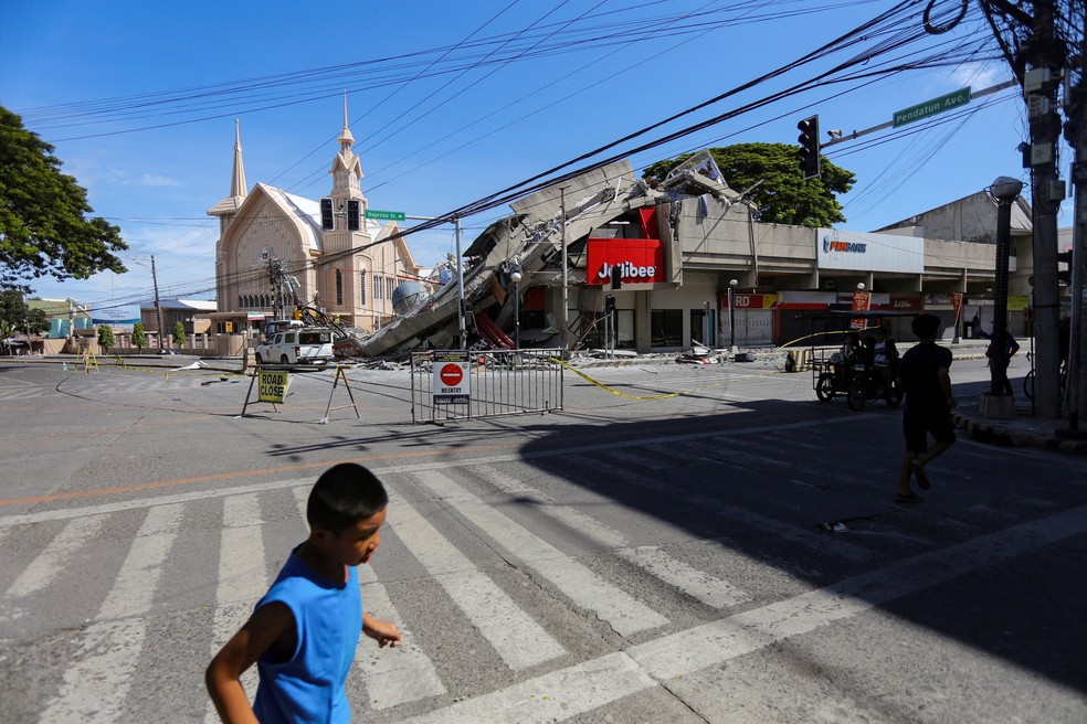 Pessoas caminham perto de um prédio desabado após o terremoto de magnitude 7,8 em General Santos, sul das Filipinas — Foto: Reuters