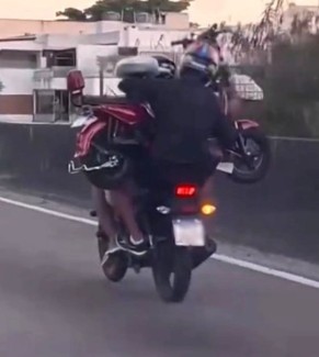 Homem pilota moto enquanto garupa carrega outro veículo no colo na Barra da Tijuca; VÍDEO 