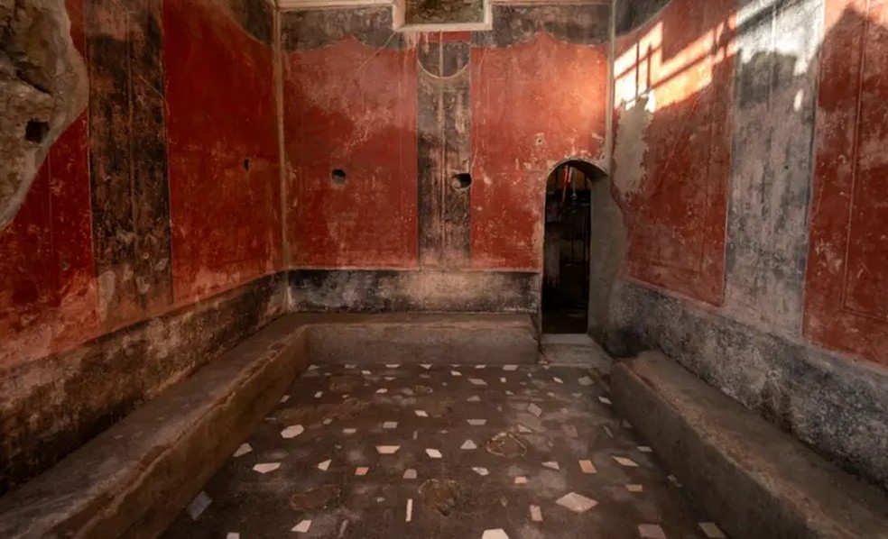 O vestiário da terma tem paredes vermelhas vibrantes, piso de mosaico e bancos de pedra. — Foto: TONY JOLLIFFE/BBC