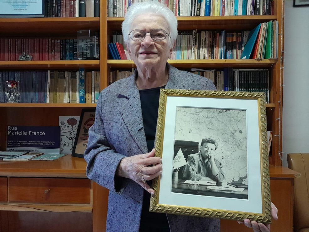 Agora deputada federal pelo PSOL, Luiza Erundina segura a foto de quando era prefeita de SP pelo PT, entre 1988 e 1992. — Foto: Rodrigo Rodrigues/g1