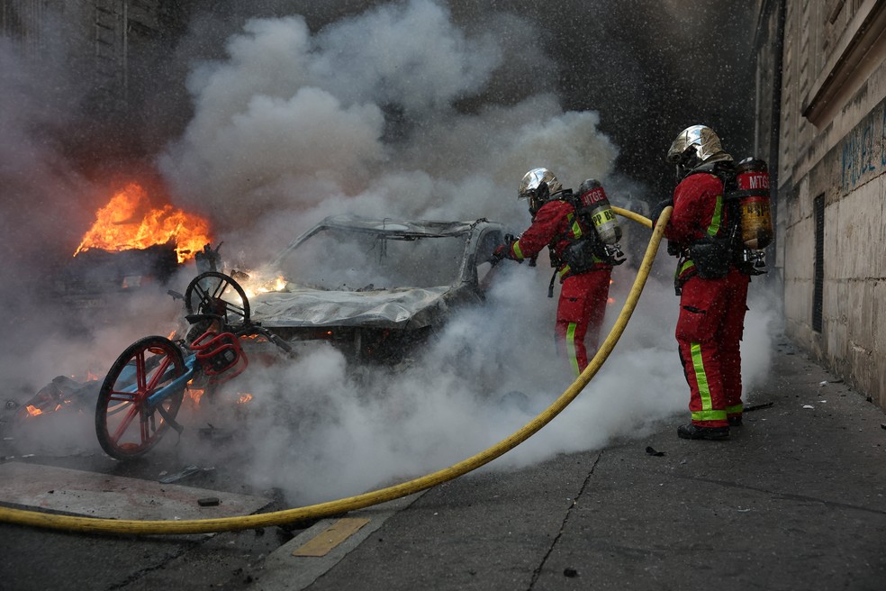 Bombeiros apagam chamas de um carro durante protestos na França — Foto: Stephanie Lecocq/Reuters