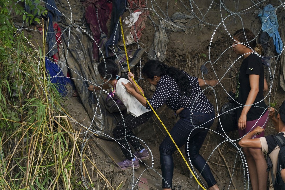 Migrantes caminham por uma barreira de arame farpado para os Estados Unidos depois de cruzar o Rio Bravo de Matamoros, México — Foto: Fernando Llano/AP