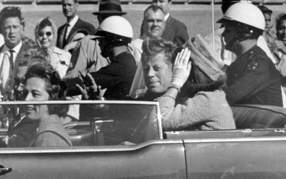 O presidente dos EUA John F. Kennedy acena de seu carro em 22 de novembro de 1963, ao lado da primeira-dama Jacqueline Kennedy, pouco antes de ser assassinado — Foto: AP Photo/Jim Altgens
