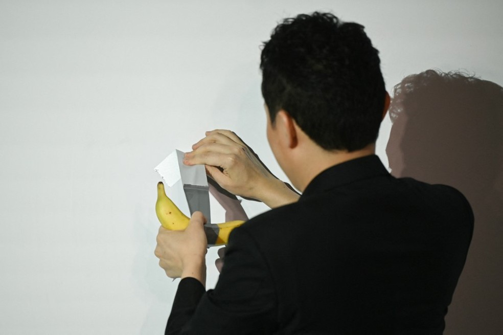 Justin Sun retira banana de obra arte polêmica que ele comprou por US$ 6,2 milhões para comê-la — Foto: Peter Parks/ AFP