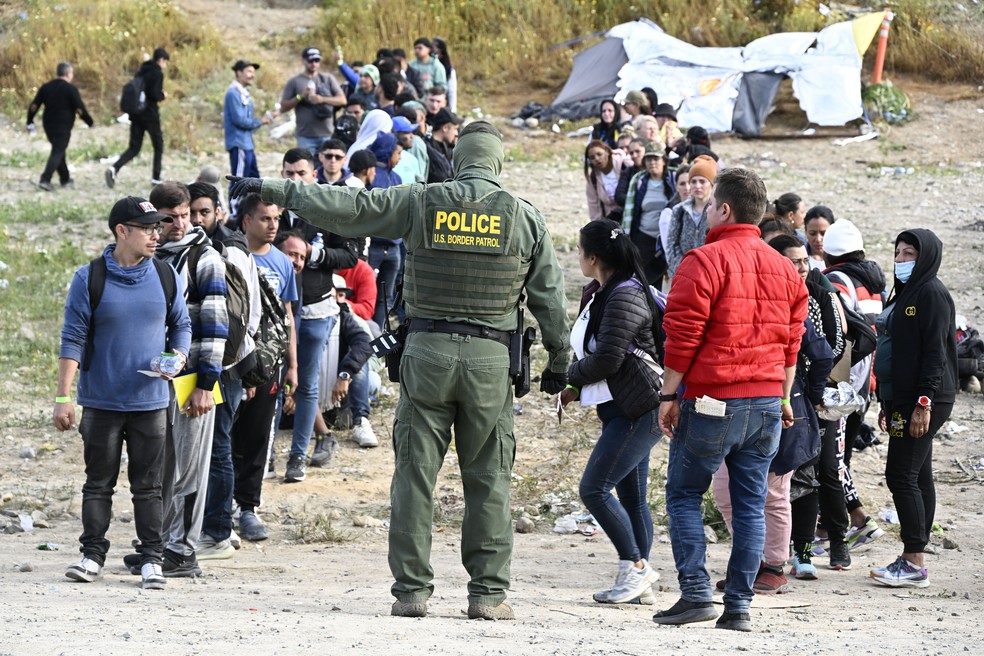 Agente de patrulha da fronteira entre EUA e México organiza migrantes próximo de Tijuana, no México — Foto: Denis Poroy/AP