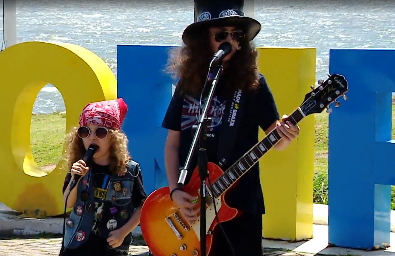 Irmãos de 12 e 5 anos encantam turistas ao tocar vestidos de membros do Guns N' Roses em pontos turísticos de Florianópolis