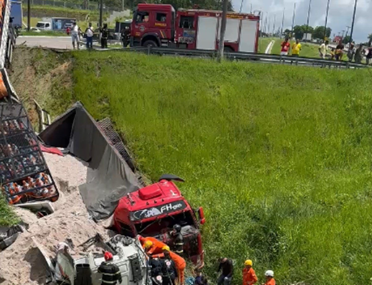 Caminhão e carreta caem em ribanceira após batida e um dos motoristas fica preso às ferragens na BR-101