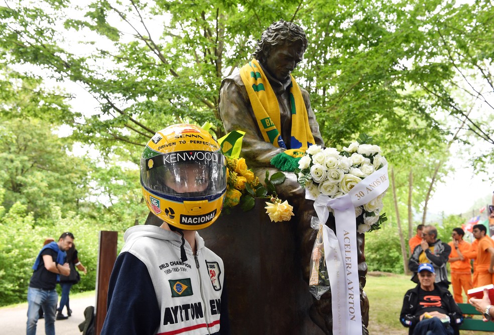 Fã de Ayrton Senna posa para foto com réplica do capacete ao lado da estátua do piloto, em Imola, na Itália — Foto: Jennifer Lorenzini/Reuters