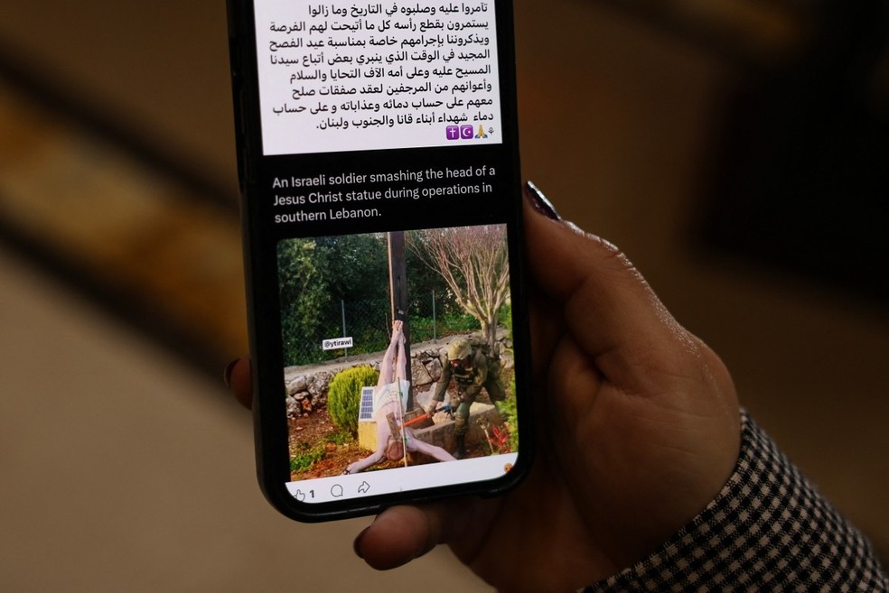 Mulher lê post em rede social mostrando depredação de imagem de Jesus Cristo por soldados israelenses — Foto: AFP