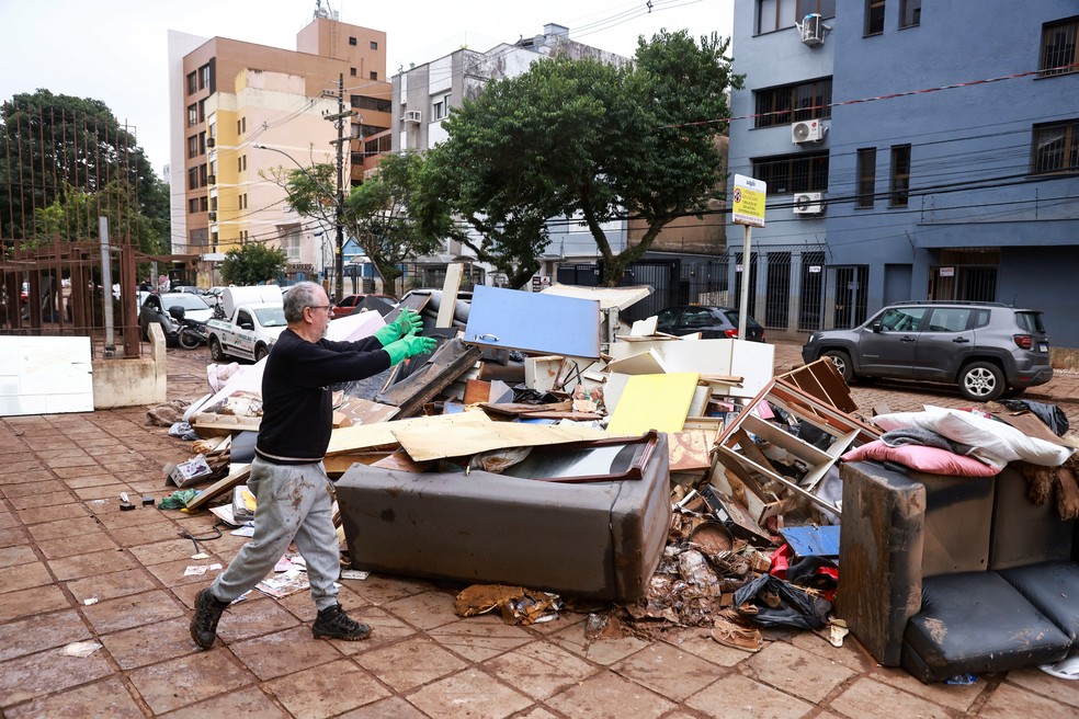 Homem descarta objetos destruídos pela enchentes após a água baixar em Porto Alegre, nesta segunda-feira (20). — Foto: Diego Vara/Reuters