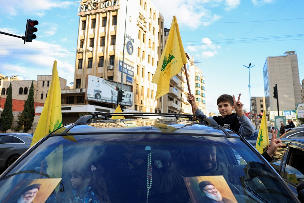 Uma criança faz um gesto enquanto segura uma bandeira do Hezbollah pela janela de um carro, na entrada dos subúrbios do Sul de Beirute — Foto: Adnan Abidi/Reuters