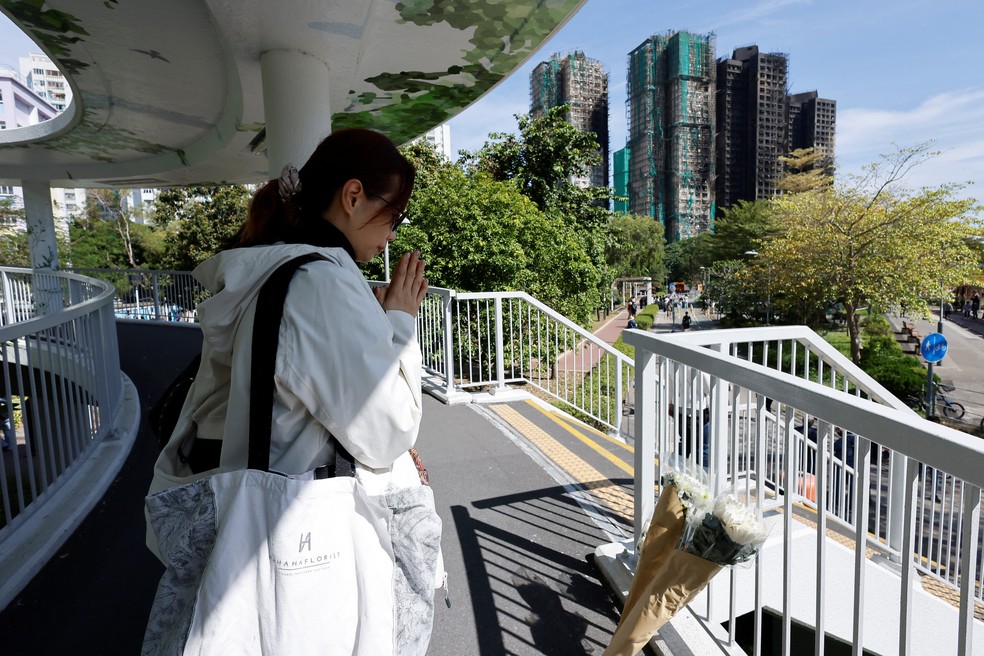Uma mulher presta luto ao lado de homenagens florais colocadas perto dos prédios queimados do complexo habitacional Wang Fuk Court, após um incêndio mortal em Tai Po, Hong Kong — Foto: Reuters/Maxim Shemetov