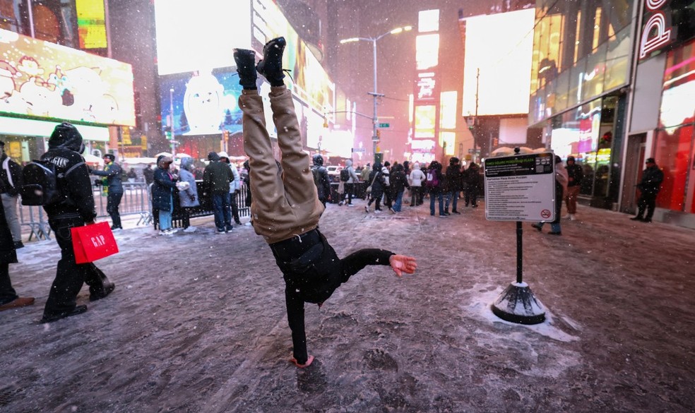 Homem faz parada de mão durante nevasca na Times Square, em Nova York, na noite de 26 de dezembro de 2025 — Foto: AFP