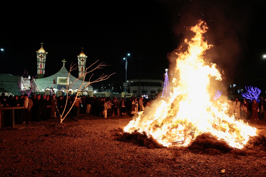 Cristãos iraquianos se reúnem em torno de fogueira em missa de Natal na igreja católica de Al-Hamdaniya, no Iraque. — Foto: Khalid al-Mousily/Reuters