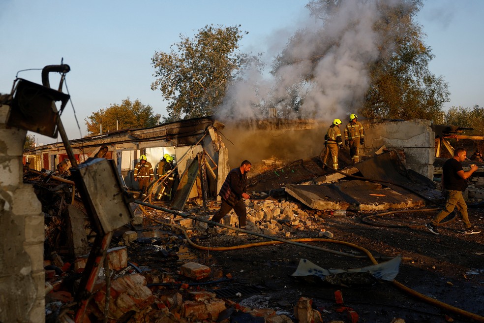 Bombeiros trabalham enquanto moradores caminham perto do local onde garagens particulares foram atingidas por um ataque de míssil russo, em meio ao ataque da Rússia à Ucrânia, em Kiev , Ucrânia — Foto: REUTERS/Valentyn Ogirenko
