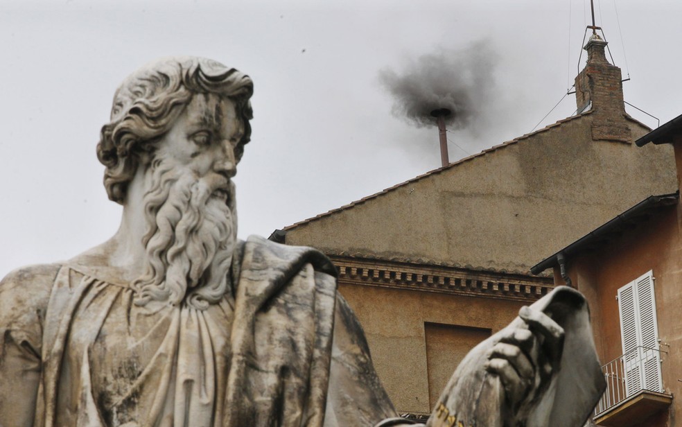 Fumaça preta sai da chaminé atrás da estátua de São Pedro, no Vaticano — Foto: Dmitry Lovetsky/AP