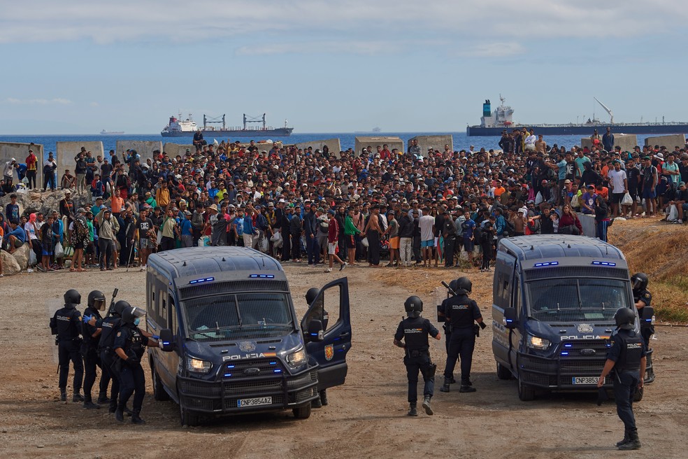 Imigrantes que cruzaram do Marrocos para Ceuta voltam a praia, um dia após serem expulsos da área, e são escoltados pela polícia. — Foto: Antonio Sempere/AP