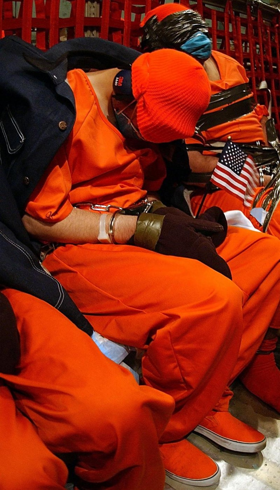Detidos suspeitos de pertencer à Al Qaeda ou ao Talibã a bordo de um avião C-141 Starlifter das forças aéreas dos EUA. Este foi o primeiro voo a enviar prisioneiros de Kandahar, no Afeganistão, para a base naval de Guantánamo. Uma bandeira americana foi colocada nas mãos de um dos detidos, além de uma jaqueta sobre os ombros dele, possivelmente para protegê-lo do frio durante o voo. — Foto: JEREMY T. LOCK/USAF via BBC