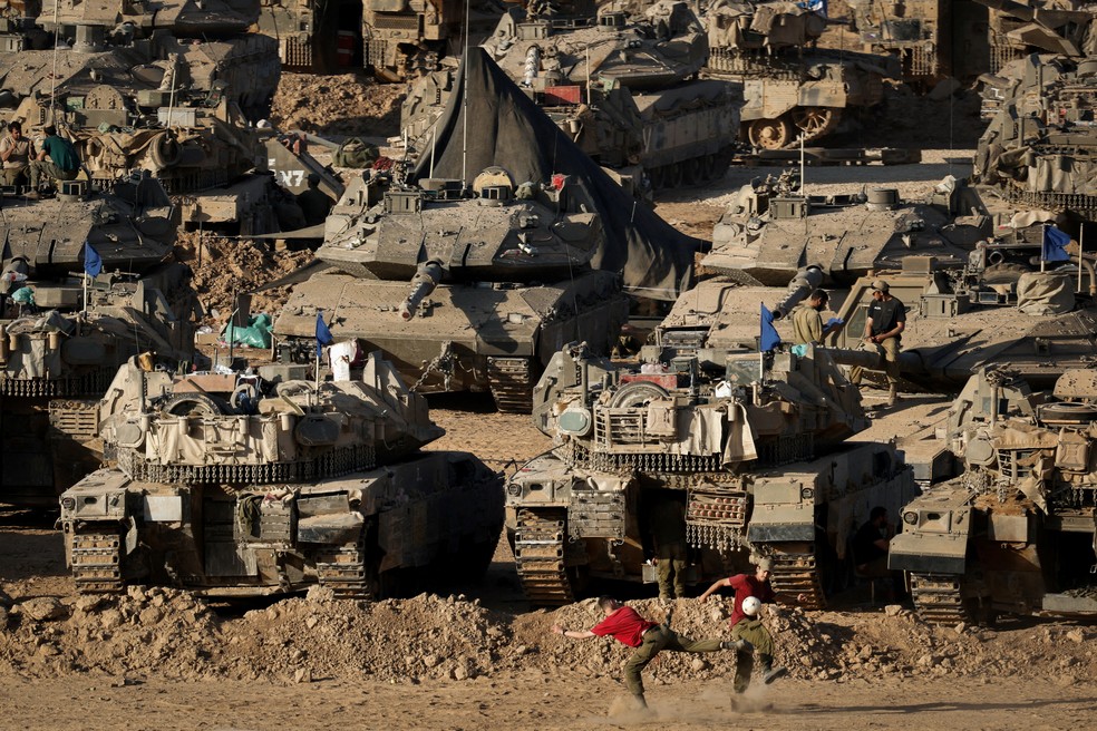 Soldados israelenses jogam futebol diante de tanques e veículos blindados de transporte de pessoal (APC), em meio ao conflito em curso entre Israel e o grupo islâmico palestino Hamas, perto da fronteira entre Israel e Gaza, em Israel — Foto: Amir Cohen/Reuters