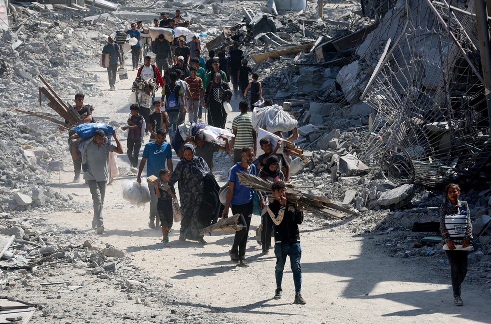 Palestinos caminham pelos escombros após a retirada das forças israelenses em Khan Younis, no sul da Faixa de Gaza, em 10 de outubro de 2025 — Foto: REUTERS/Ramadan Abed