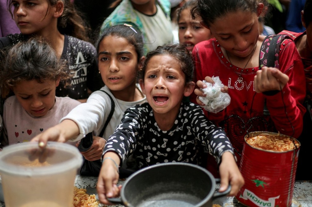Menina chora enquanto aguarda que panela seja preenchida com alimento em Gaza — Foto: Eyad BABA / AFP