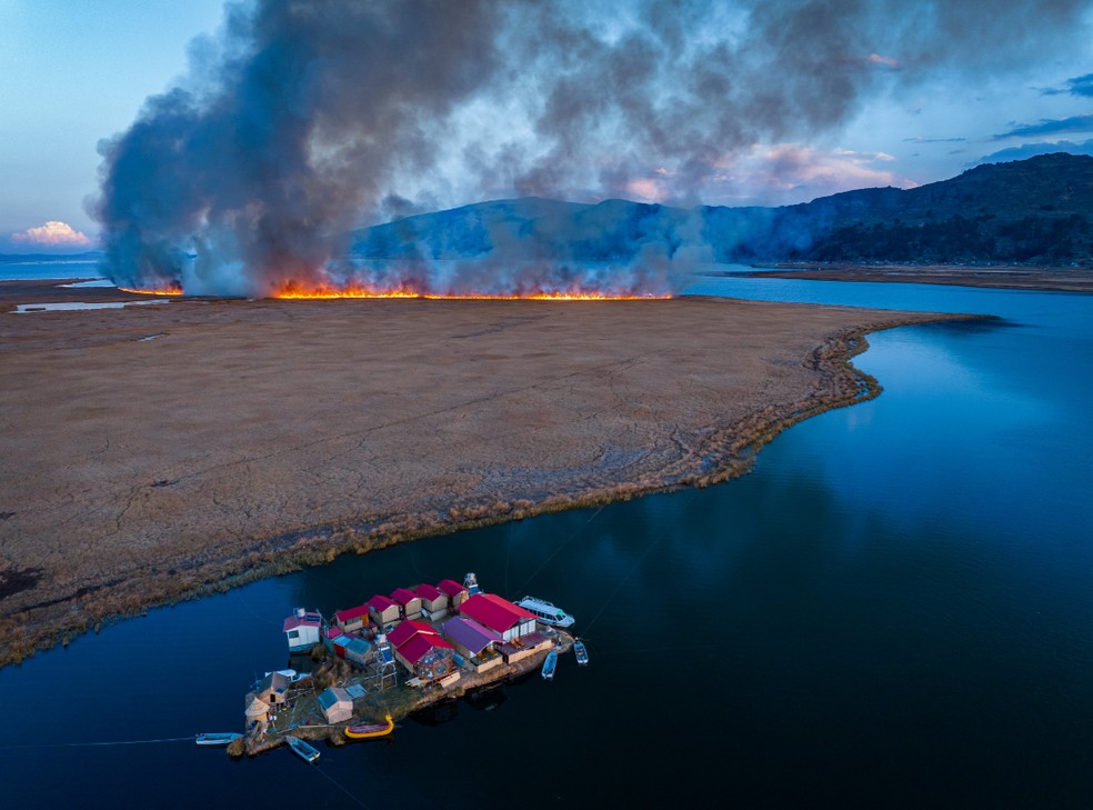 Uma pacata vila flutuante localizada nas plácidas margens do Lago Titicaca, situado na fronteira entre o Peru e a Bolívia, na Cordilheira dos Andes, em contraste com o perigo iminente de um incêndio florestal. — Foto: Yan Li (China)/World Photography Organisation