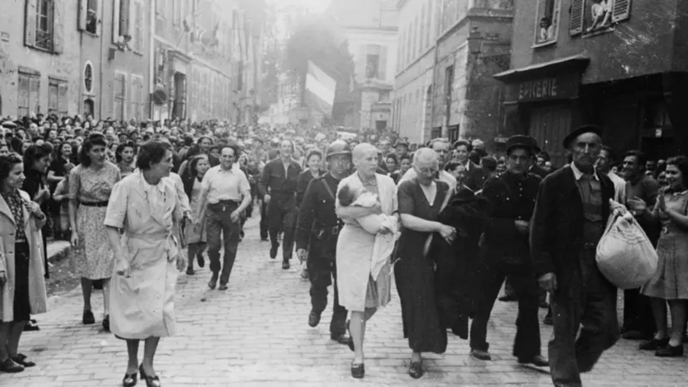 Na fotografia de Robert Capa, uma jovem mãe com a cabeça raspada como forma de punição é conduzida por uma multidão — Foto: Getty Images / BBC